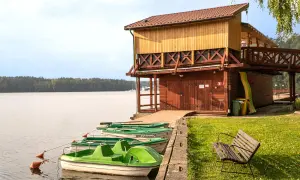 Łódki przy pomoście, drewniana przystań i zielona trawa. Wrzosowa Góra Ruciane Nida zaprasza na wodne przygody.