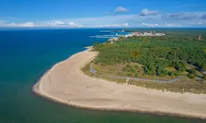Półwysep Helski: piaszczysta plaża, turkusowe morze i las. W oddali widać miasteczko i port. Atrakcje tego miejsca zachwycają.
