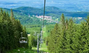 Wjazd kolejką linową na wysoką kopę szlak. Widok na zielone lasy i zabudowania w oddali.