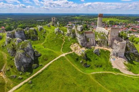 Ruiny zamków na wapiennych skałach w **parku krajobrazowym Orlich Gniazd**. Zielone wzgórza i błękitne niebo.