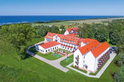 Hotel Mona Lisa Kołobrzeg z widokiem na morze. Białe budynki z czerwonymi dachami otoczone zielenią.