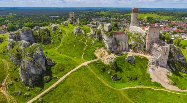 Ruiny zamków na wapiennych skałach w **parku krajobrazowym Orlich Gniazd**. Zielone wzgórza i błękitne niebo.