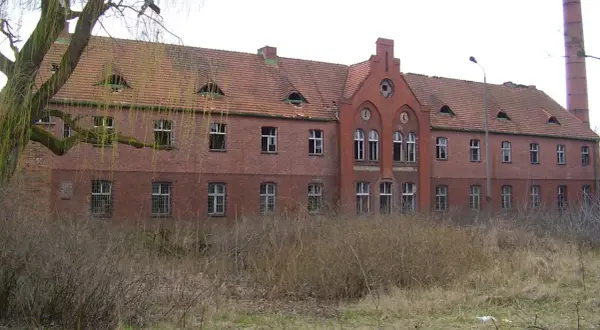 Opuszczony budynek z cegły, zniszczony dach i wybite okna. Miejsce to mogłoby być jednym z nawiedzonych miejsc w Polsce, budzącym grozę.
