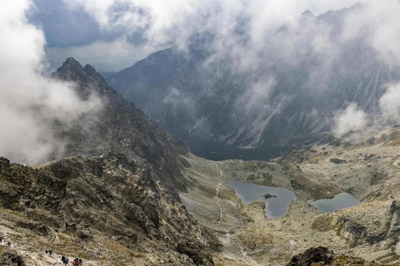 Widok na Tatry z mgłą, idealne miejsce na pierwsze górskie wędrówki. Szlak prowadzi w dół do malowniczych jezior.