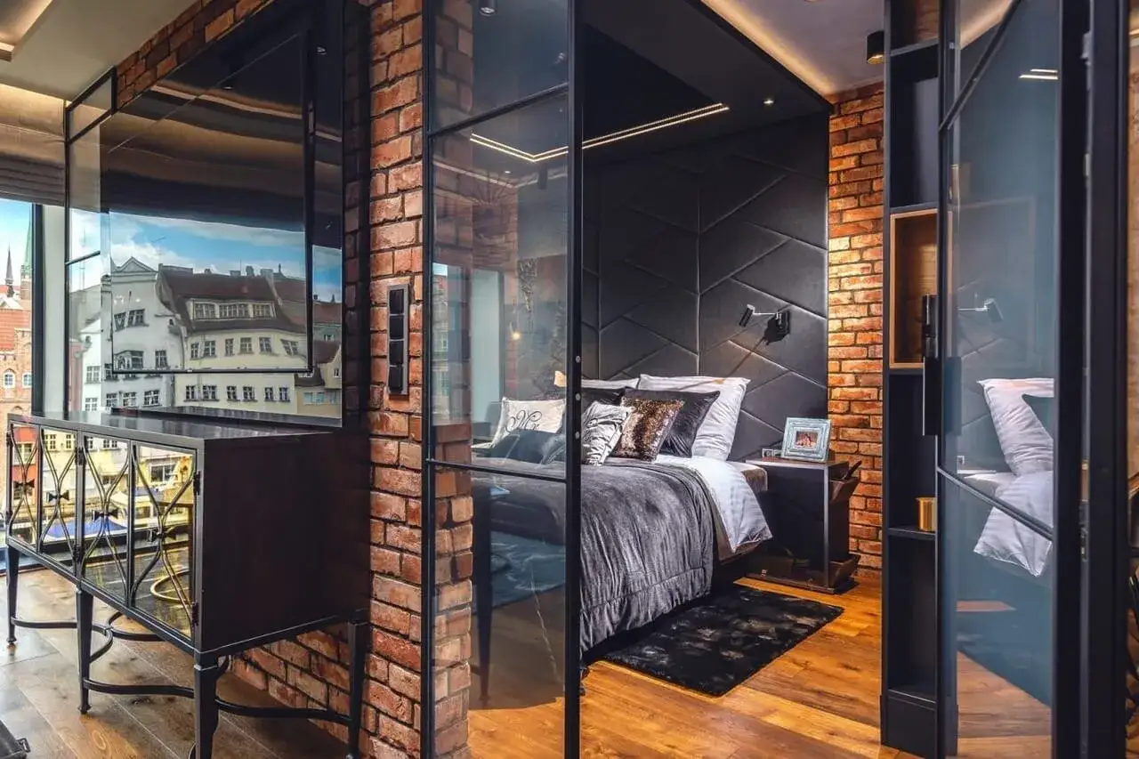 Nowoczesny green loft z cegłą i szkłem. Sypialnia z wygodnym ł&oacute;żkiem i widokiem na miasto.