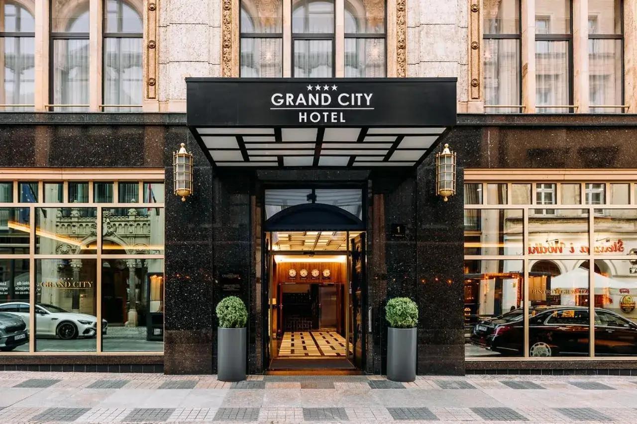 Elegancki grand city hotel z lśniącym wejściem, ozdobionym złotymi lampami i zielonymi roślinami.