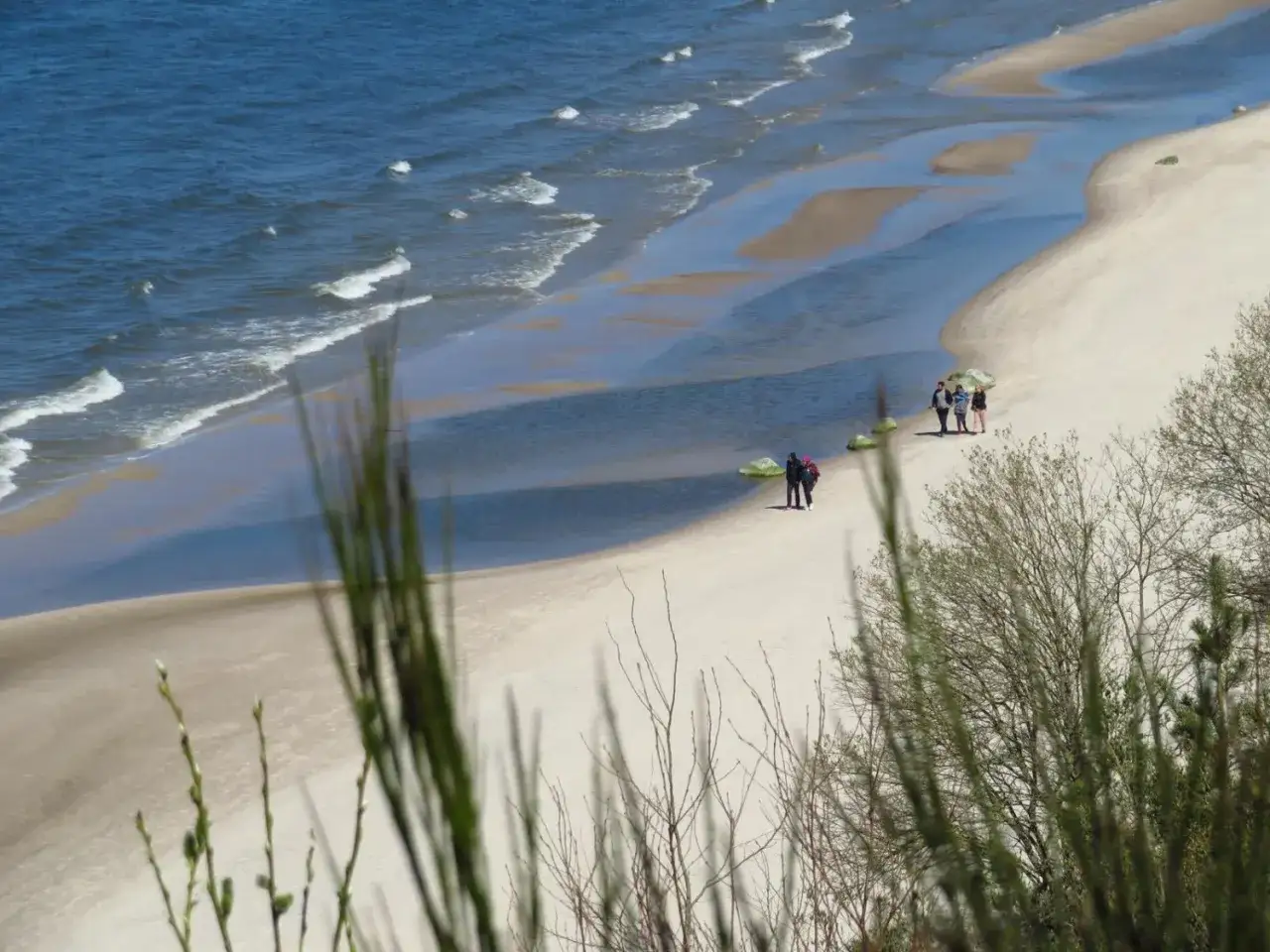 Spacer po piaszczystej plaży, gdzie woda tworzy malownicze kałuże. W oddali widać grupę ludzi. Dębina plaża.