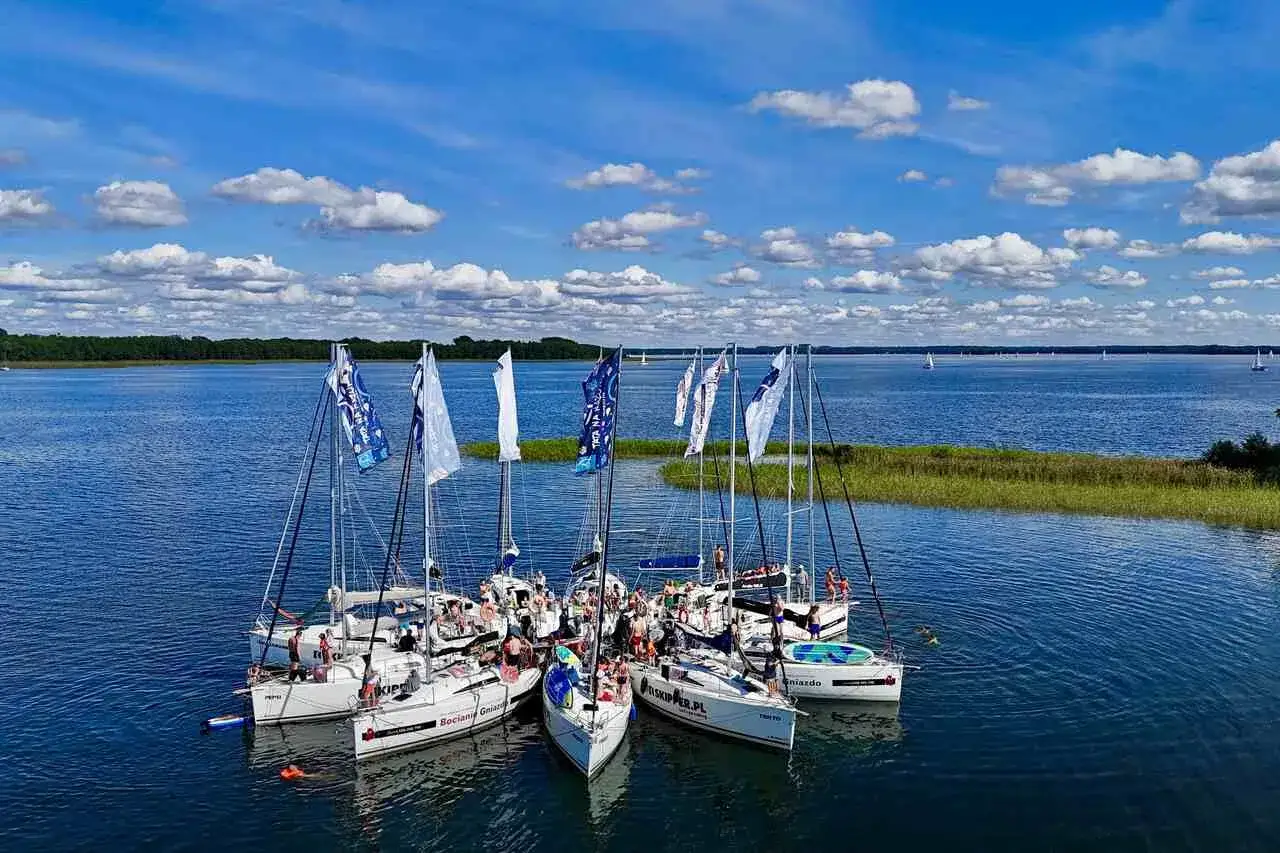 Żagl&oacute;wki na Mazurach, idealne mazury atrakcje. Ludzie na pokładach, błękitne niebo i białe chmury.