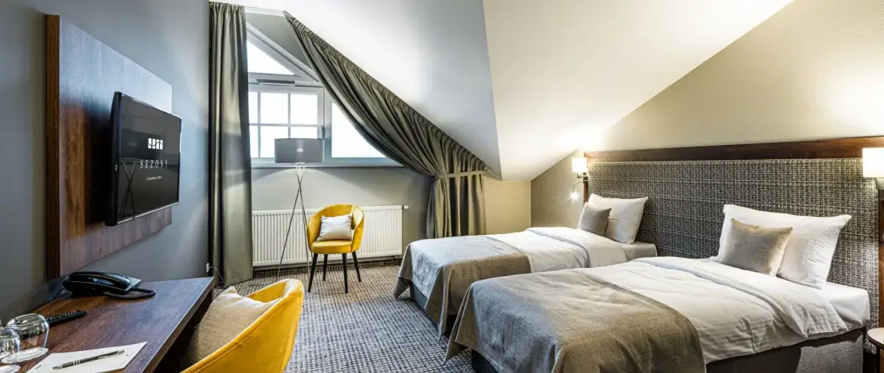 Pok&oacute;j hotelowy z dwoma ł&oacute;żkami, ż&oacute;łtym fotelem i biurkiem. Idealne miejsce na nocleg, zapewniające komfortowe gwiazdki w hotelach.