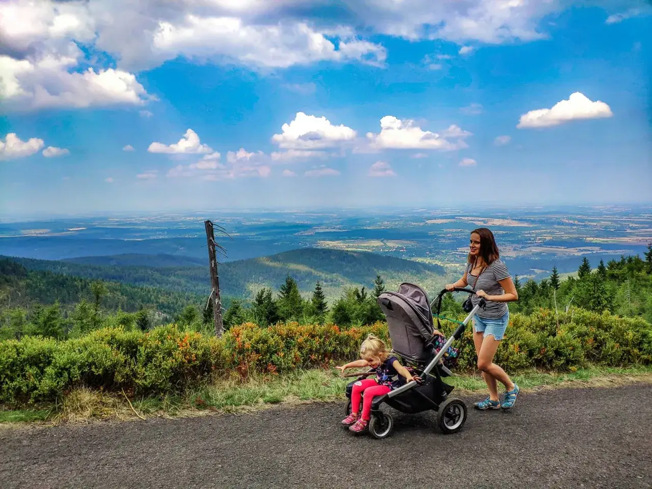 Mama z c&oacute;rką na spacerze, gdzie w g&oacute;ry z w&oacute;zkiem. Piękny widok na dolinę i chmury.