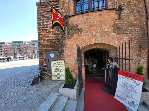 Gdańska Baszta Tajemnic zaprasza do swojego mrocznego świata. Figurka postaci w stroju z epoki stoi przed wejściem.