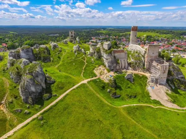 Ruiny zamków na wapiennych skałach w **parku krajobrazowym Orlich Gniazd**. Zielone wzgórza i błękitne niebo.
